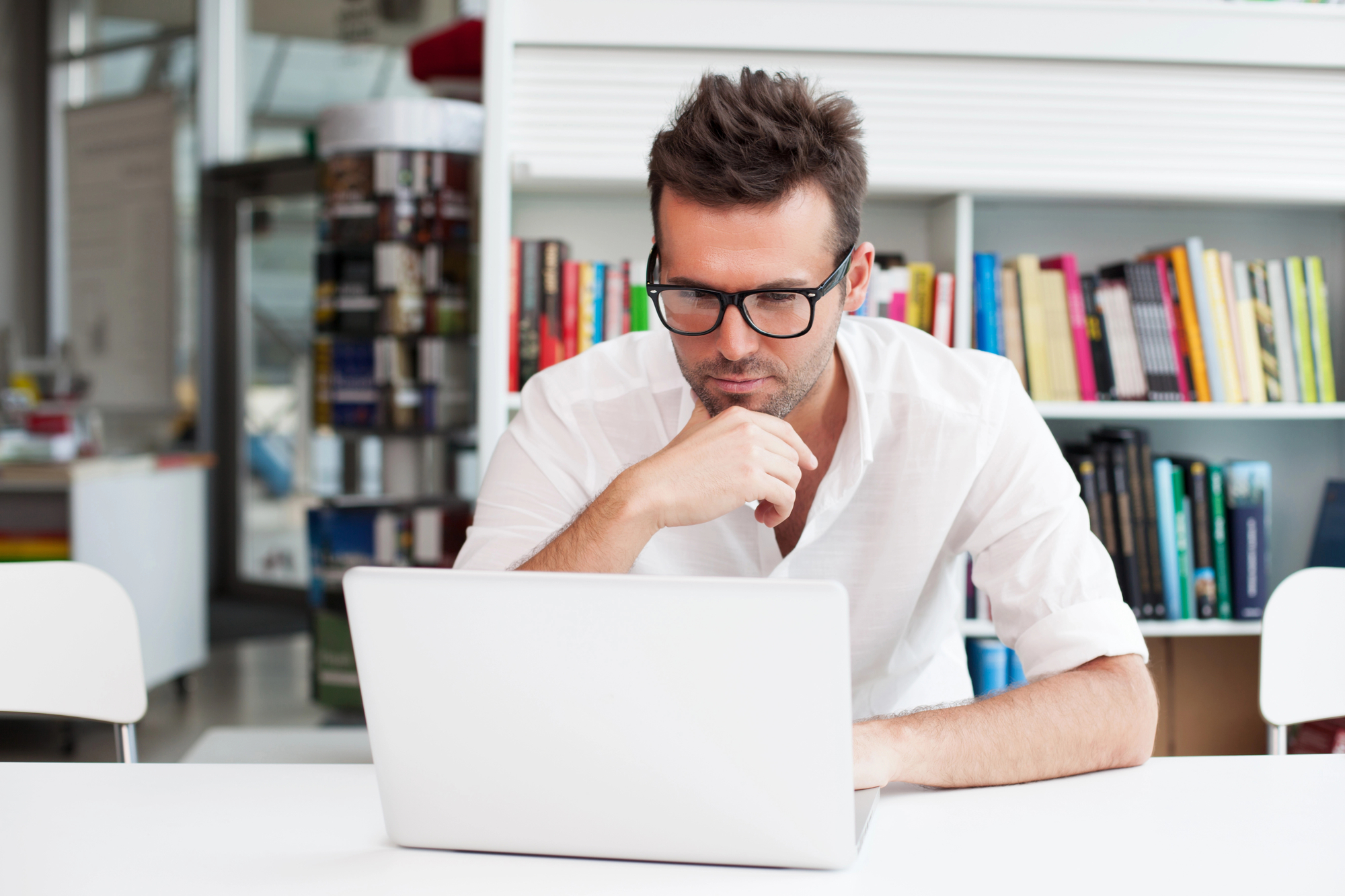 man van een jaar of 30 met een bril en een wit t-shirt zit achter een laptop