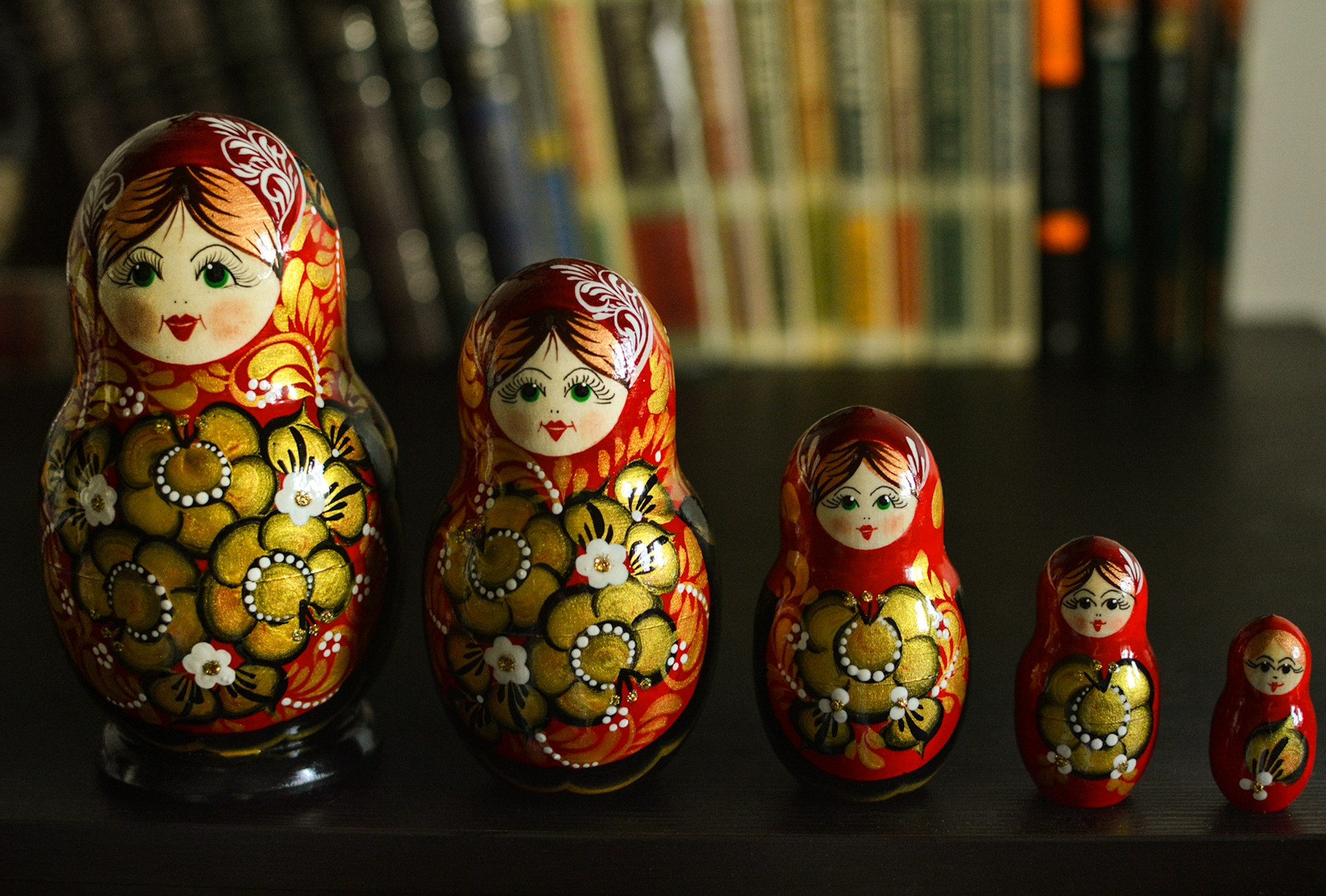 een reeks traditionele Russische Matroesjka-poppen, variërend in grootte van groot naar klein, met kleurrijke bloemmotieven en gedetailleerde gezichten. Op de achtergrond zijn boeken zichtbaar.